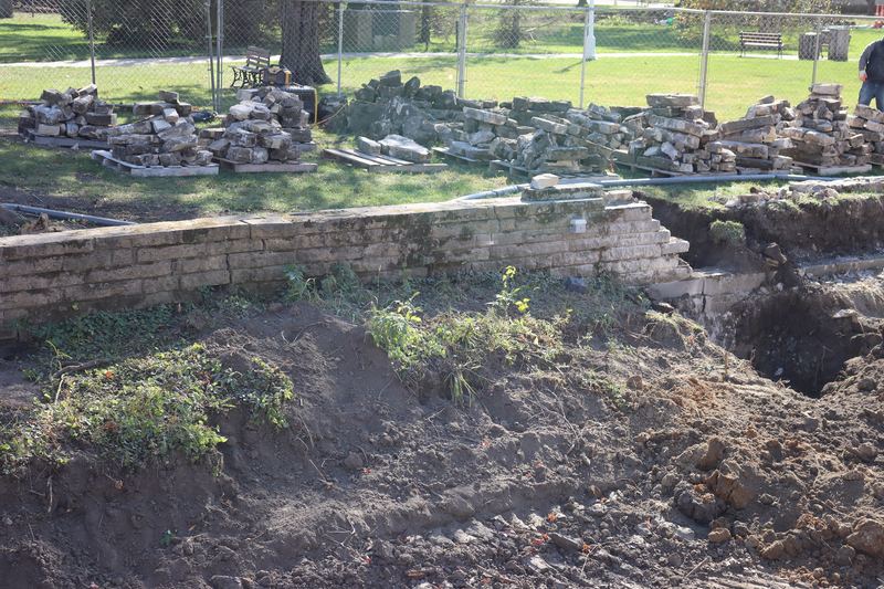 Old stone retaining wall runs from left to right in the midground of image. The right one third of the wall has been disassembled and stones